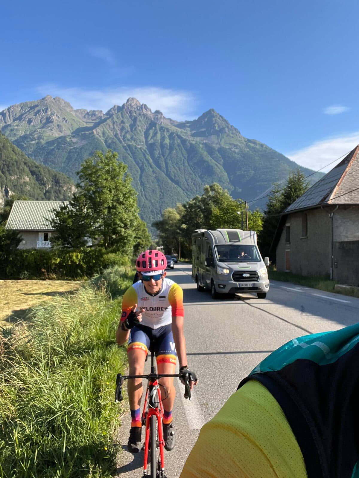 Olen Lokkesmoe climbing an Alpine mountain road in Velobrew cycling kit with dramatic mountain peaks in the background
